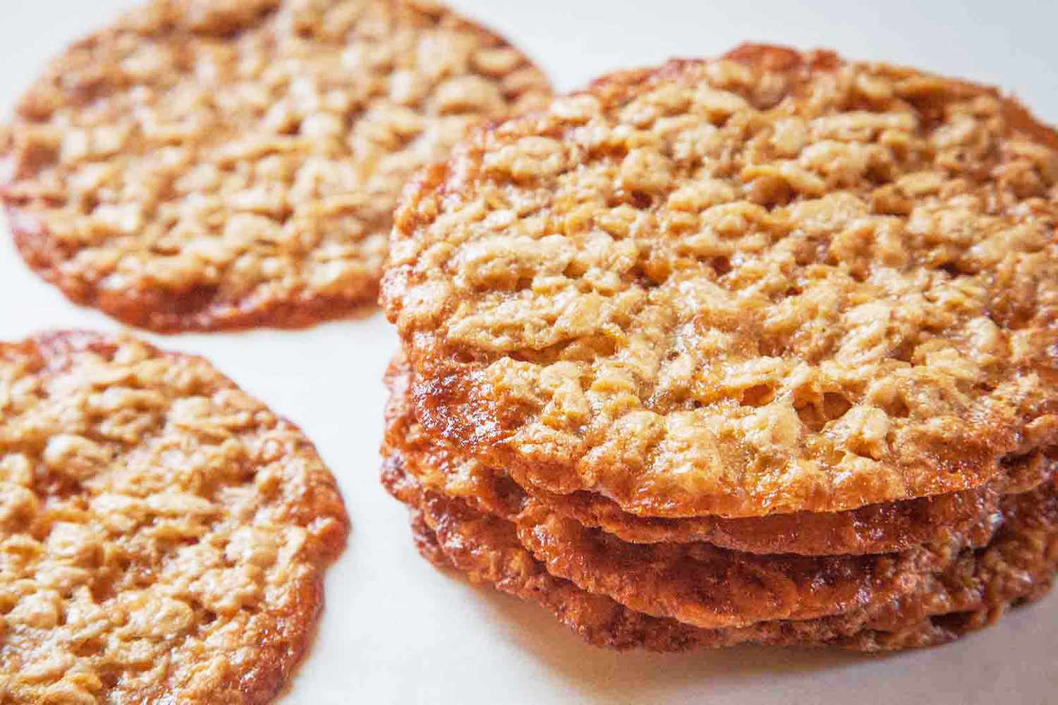 A stack of oatmeal lace cookies and additional cookies arranged nearby