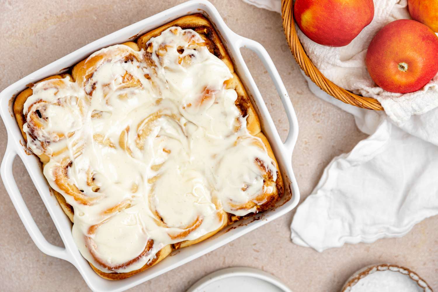 Apple Cinnamon Rolls with Cream Cheese Frosting Next to a Bowl of Apples