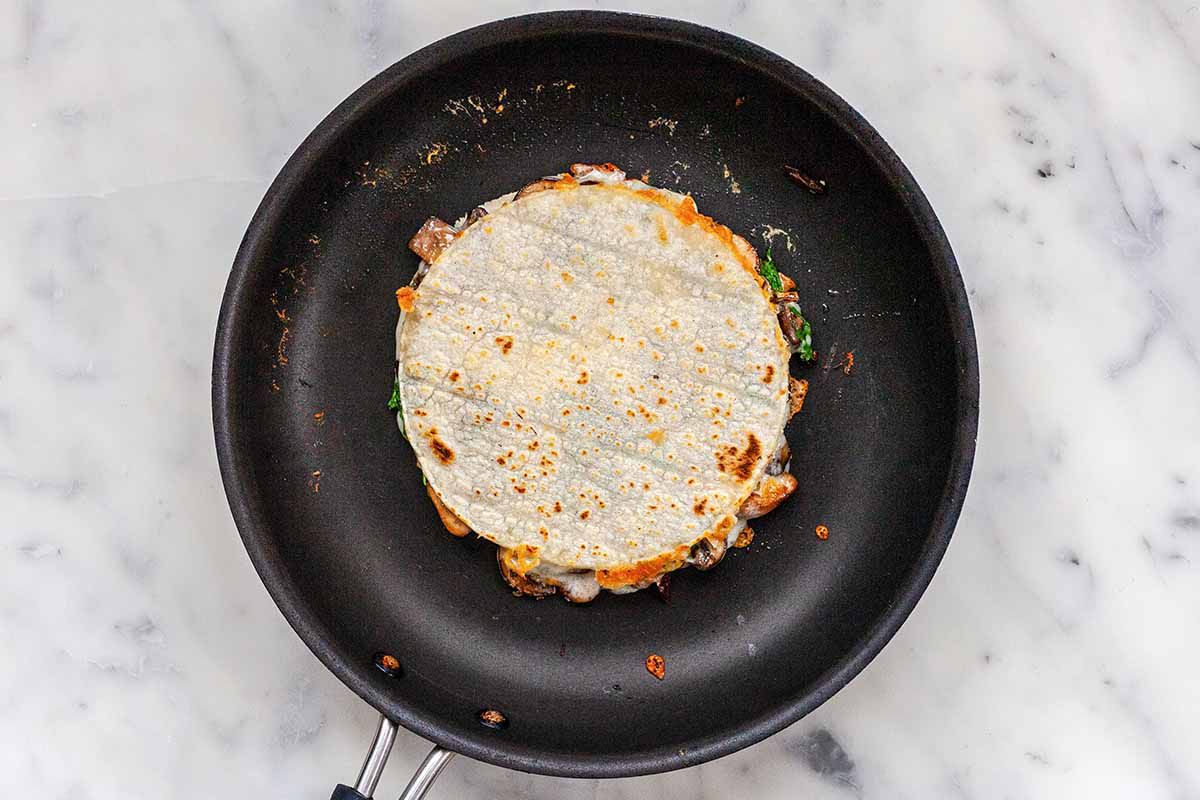 How to Make Quesadillas Vegetarian - cooked tortillas filled with cheese and mushooms in black skillet.