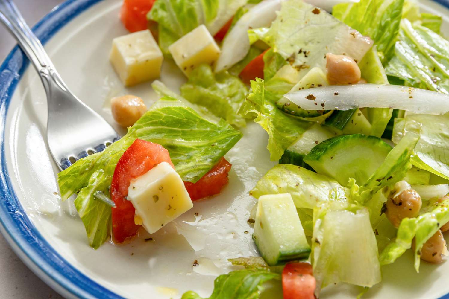 A plate with Sicilian chopped salad containing lettuce tomato cheese cucumber and chickpeas with a fork on the side