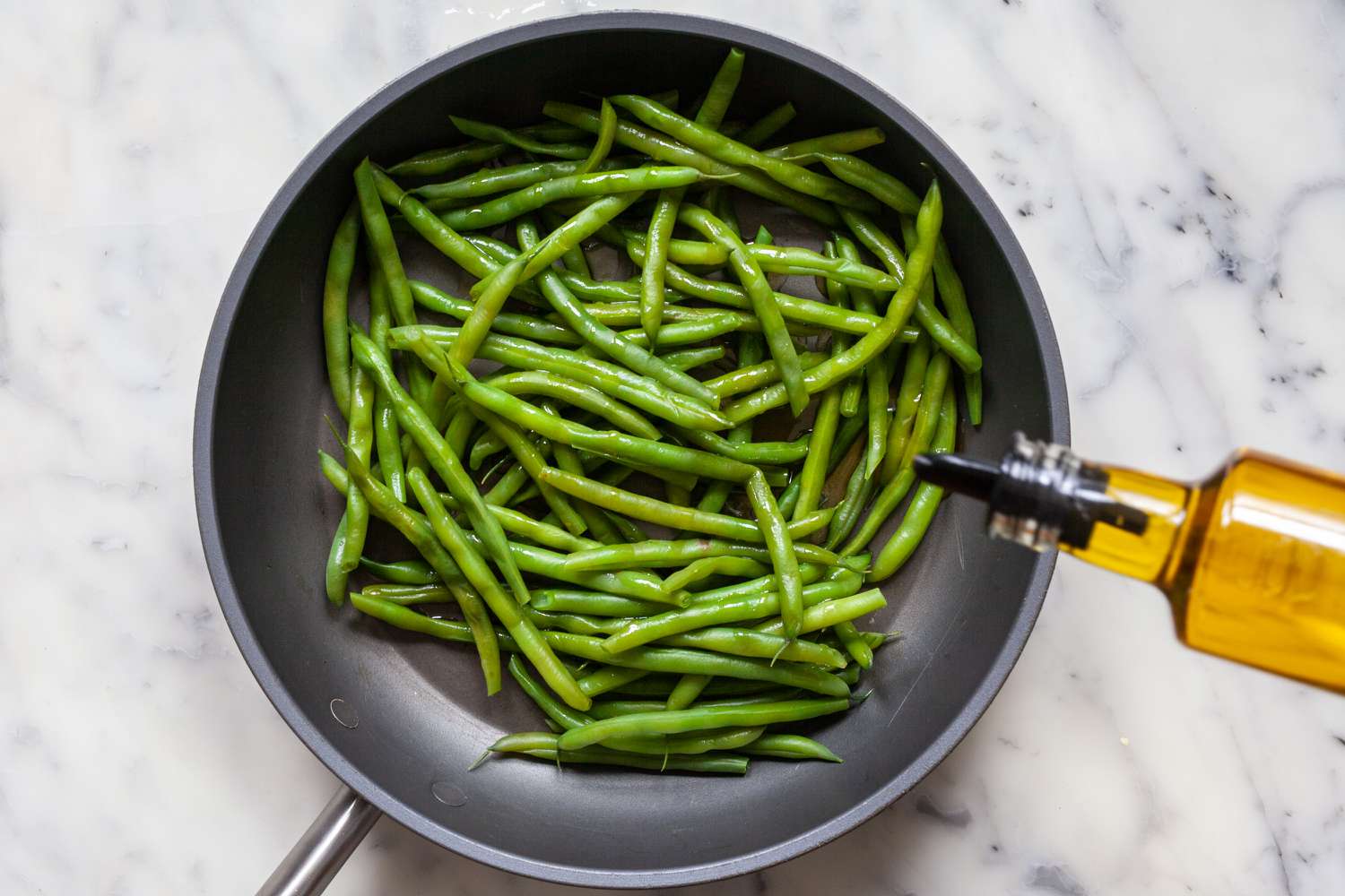 Adding oil to green beans to make Blistered Green Beans with Gochujang.