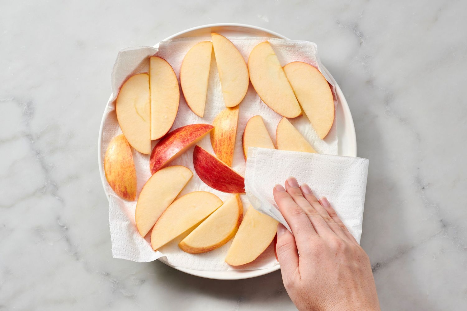 Sliced apples on a plate being blotted with a paper towel by a hand