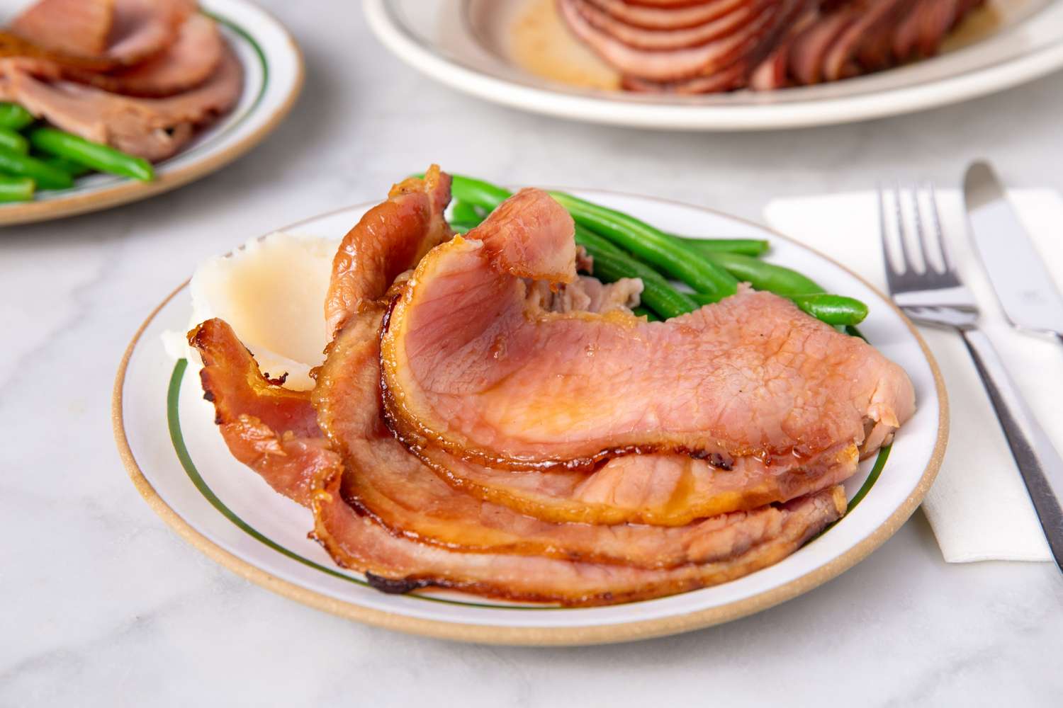 Sliced cooked ham served on a plate with green beans and a white napkin nearby