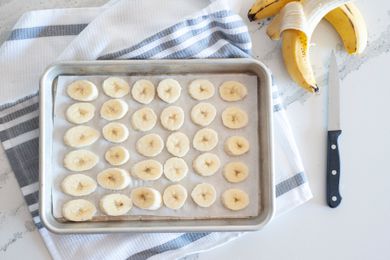 Slices of bananas on a half sheet pan ready for freezing