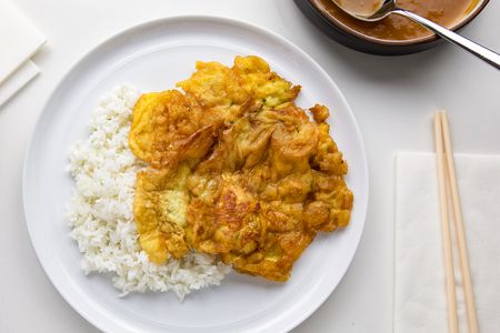 Egg Foo Young on a Plate with Jasmine Rice at a Table Setting with Chopsticks on a Napkin and a Pot of Sauce