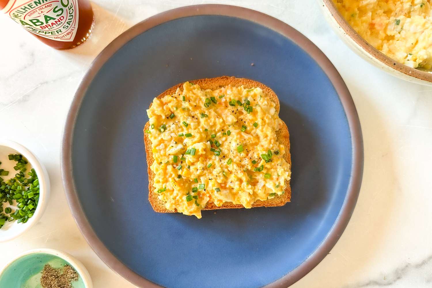 a plate with toast topped with The 5-Ingredient Egg Salad Served at Royal Tea, various ingredients on the side