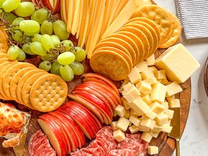 An arrangement of fruit cheese crackers and deli meats on a wooden board
