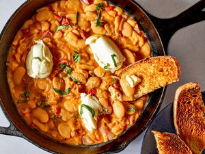Overhead shot of Tuscan butter beans in a skillet topped with dollops of ricotta toasted bread on the side