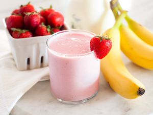 A glass with a strawberry banana smoothie and strawberry and banana fruits in the background
