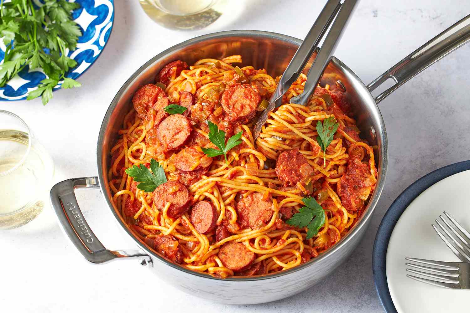 A pot of cooked spaghetti with sausage in sauce garnished with parsley
