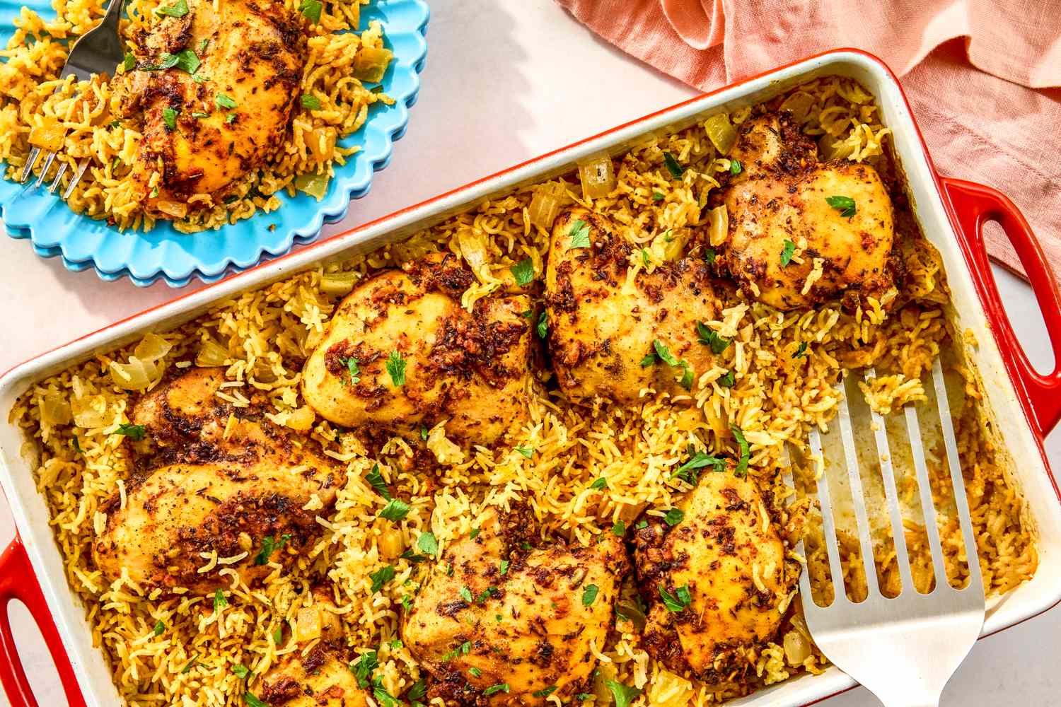 A baking dish with baked chicken and rice yellow and garnished with fresh herbs served with a portion on a blue plate