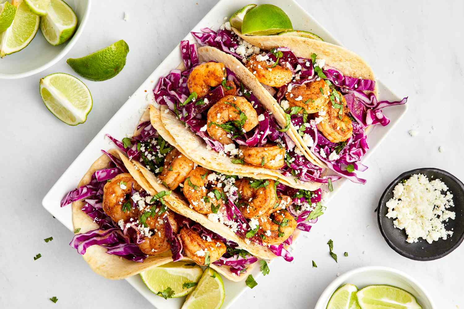 Blackened Shrimp Tacos and Lime Wedges on a Plate Surrounded Bowls of More Lime Wedge and a Bowl of Queso Fresco