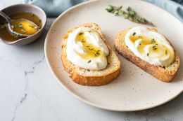 Two Pieces of Whipped Ricotta Toast Topped with Honey Next to a Bowl of Thyme Honey