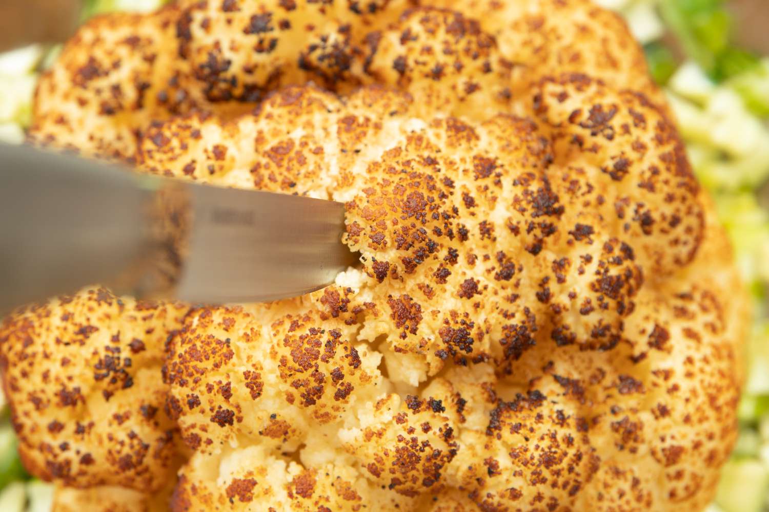 Knife Piercing the Smoked Whole Cauliflower with Spiced Soy Butter and Satay Sauce