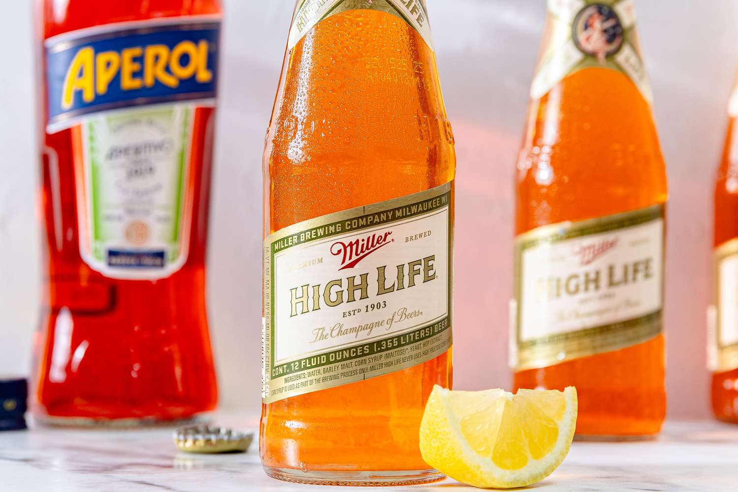 Miller High Life beer bottle with a lemon wedge Aperol bottle in the background