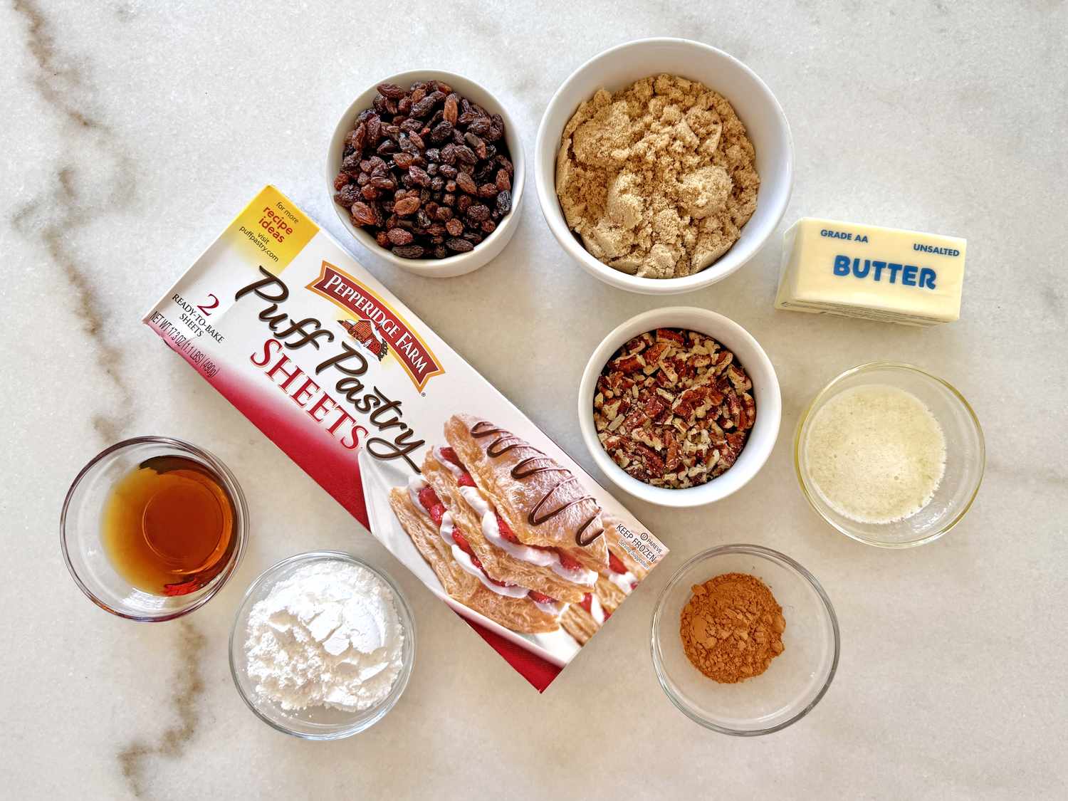 Ingredients arranged for making sticky buns including puff pastry brown sugar butter pecans raisins vanilla extract and spices