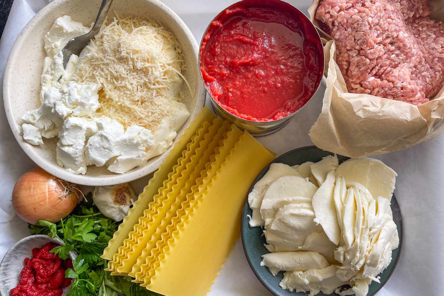 Lasagna ingredients including ricotta parmesan tomato sauce ground meat mozzarella lasagna noodles onion parsley and garlic