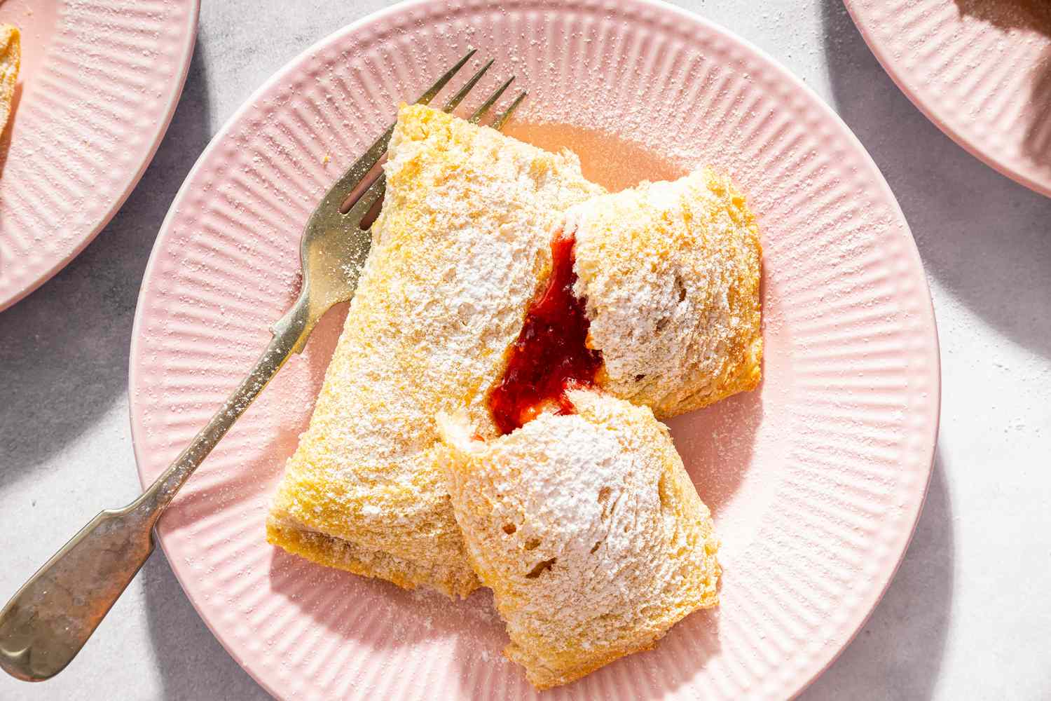 Toast Pies on dessert plate, dusted with powdered sugar, one torn open to show red filling