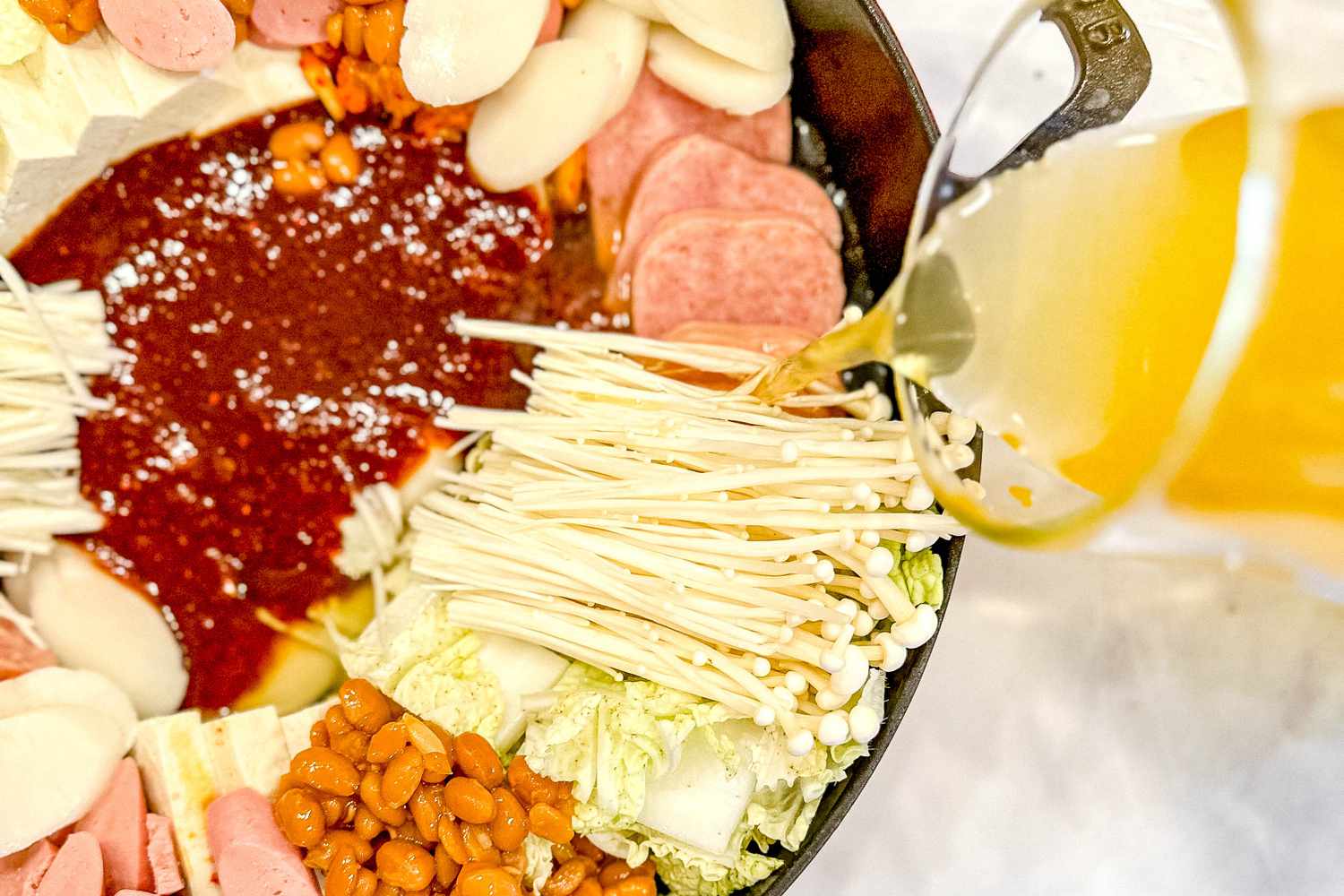 Chicken broth poured around the edges of the pot, over the solid ingredients for Korean army base stew