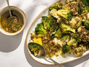 Overhead shot of a bowl with bagna cauda next to a plate with broccoli and cauliflower topped with the condiment