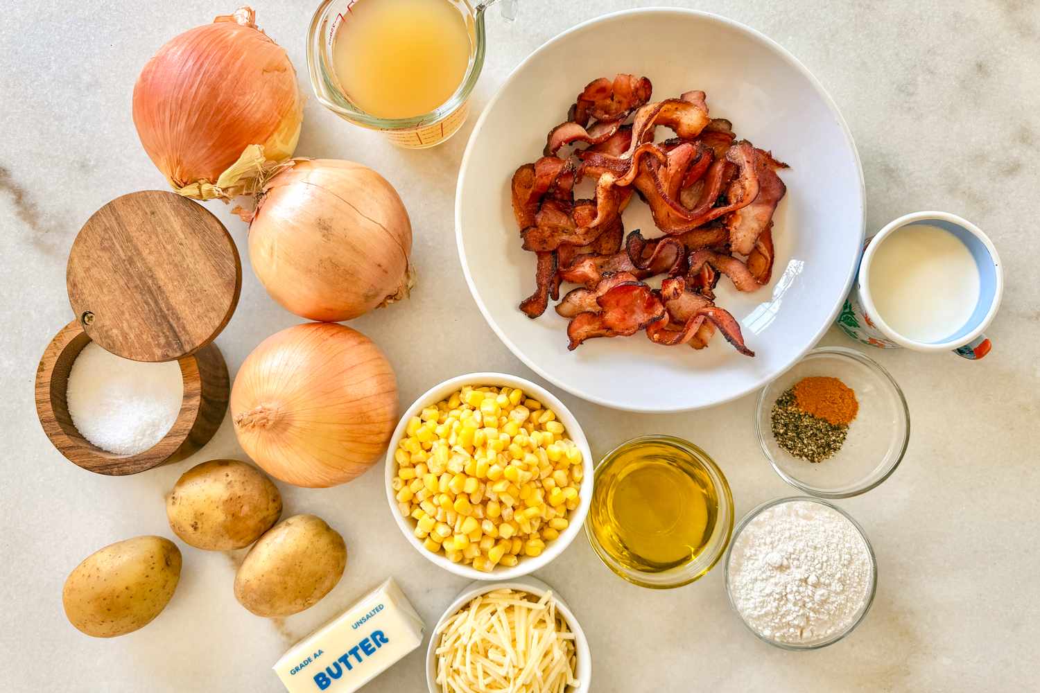 Ingredients for corn chowder laid out on a surface including bacon onions corn potatoes and seasonings