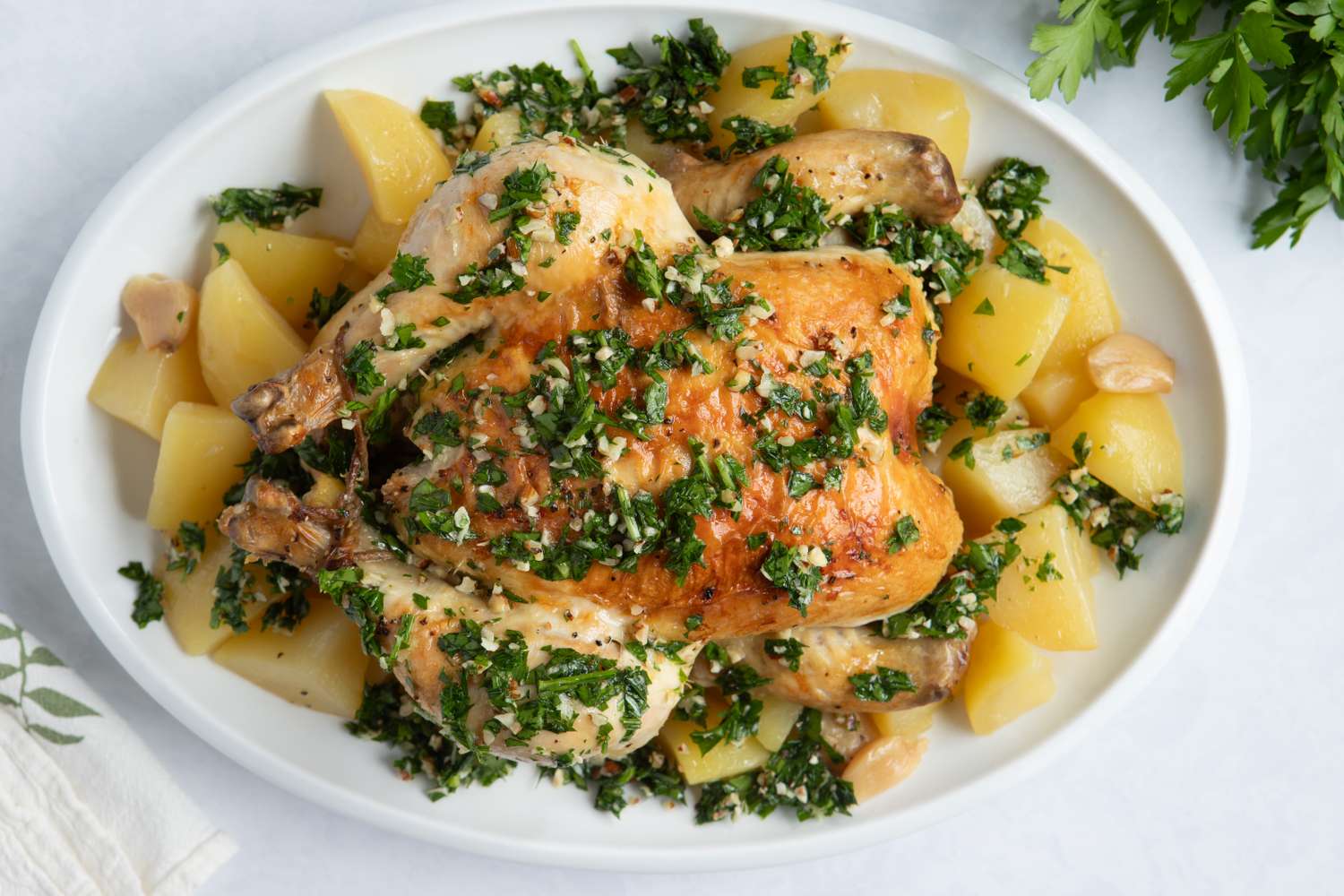 A roasted chicken garnished with fresh herbs and served with potato pieces on a white plate