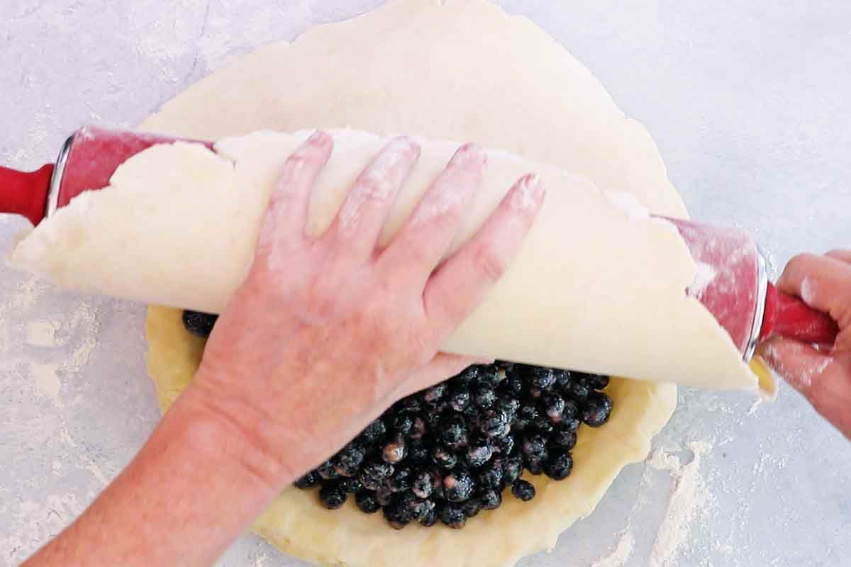 Top of the pie crust being placed over the pie with a rolling pin