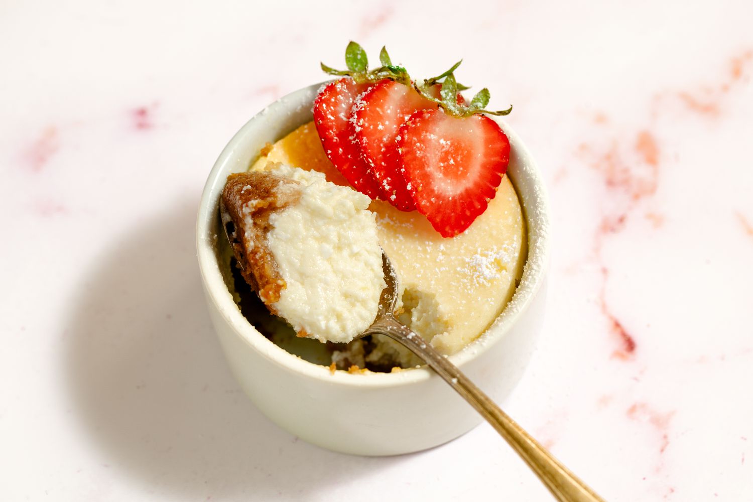 A cheesecake baked in a ramekin with a spoonful taken out and a strawberry garnish on top