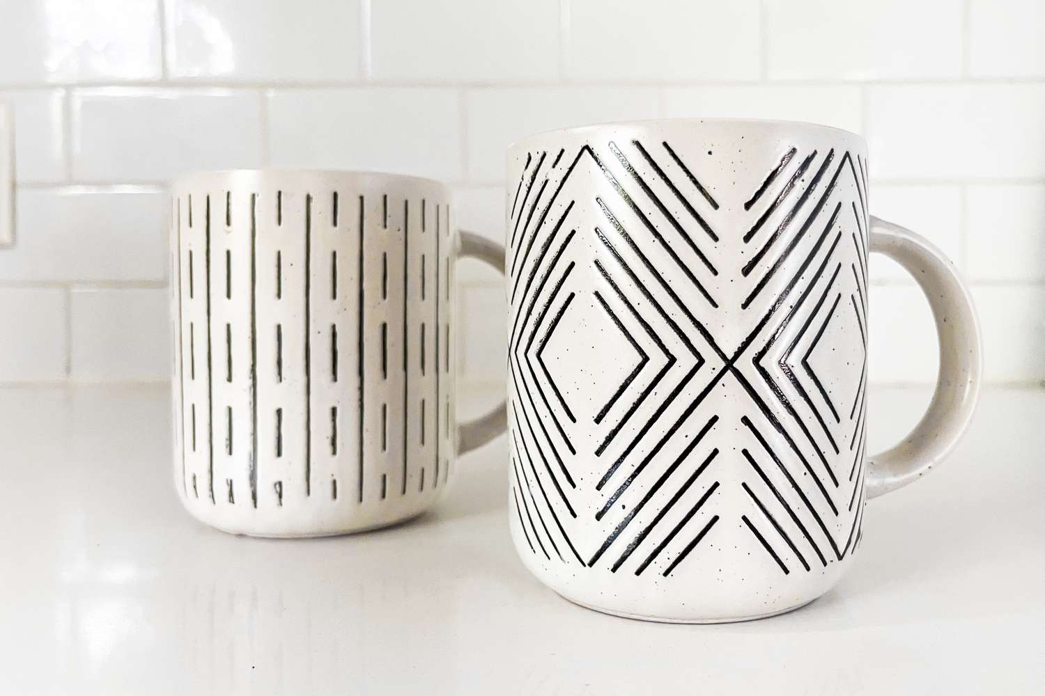 Two white Dollar Tree mugs with black markings, on a white counter top