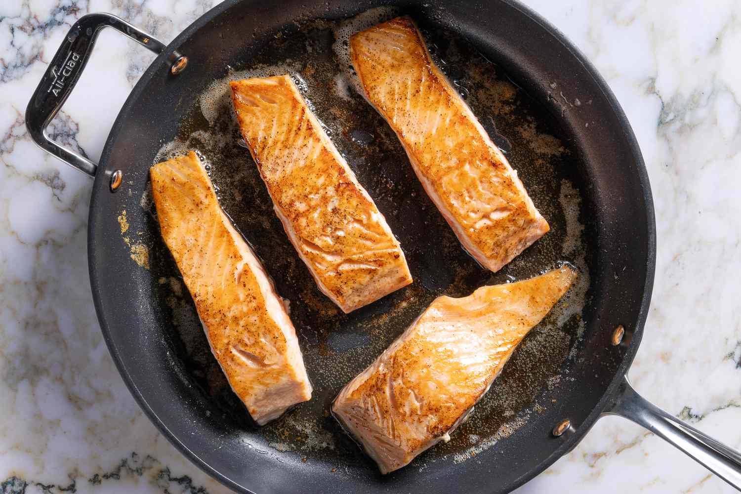 overhead view of salmon fillets, skin-down in a skillet, golden brown on top - Salmon Piccata