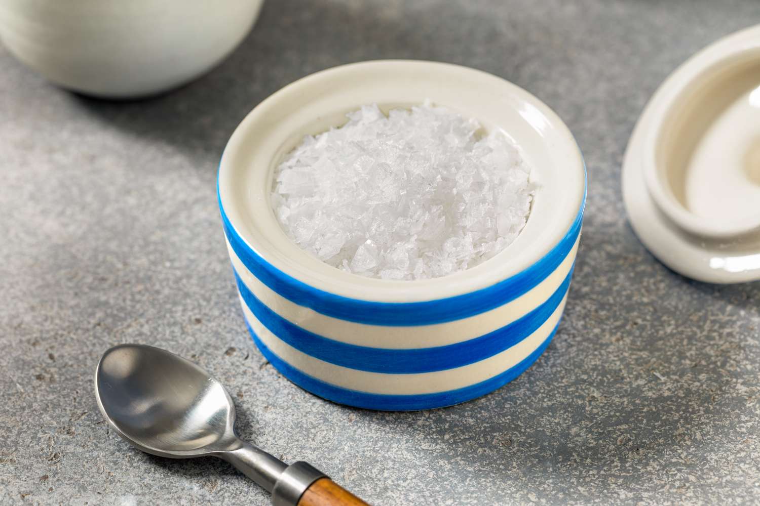 A ceramic container with coarse salt next to a small metal spoon on a countertop