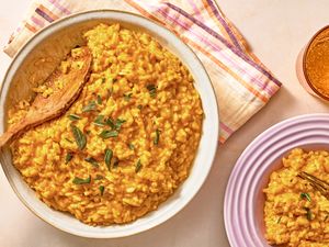 Bowl of pumpkin risotto with herbs and a wooden spoon