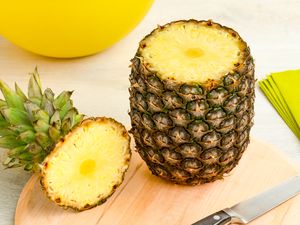 Pineapple with top removed showing interior flesh on a wooden cutting board with a knife nearby