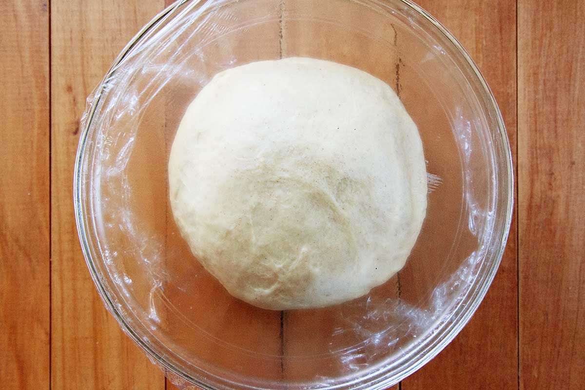 A risen king cake dough in a glass bowl on a wooden table.