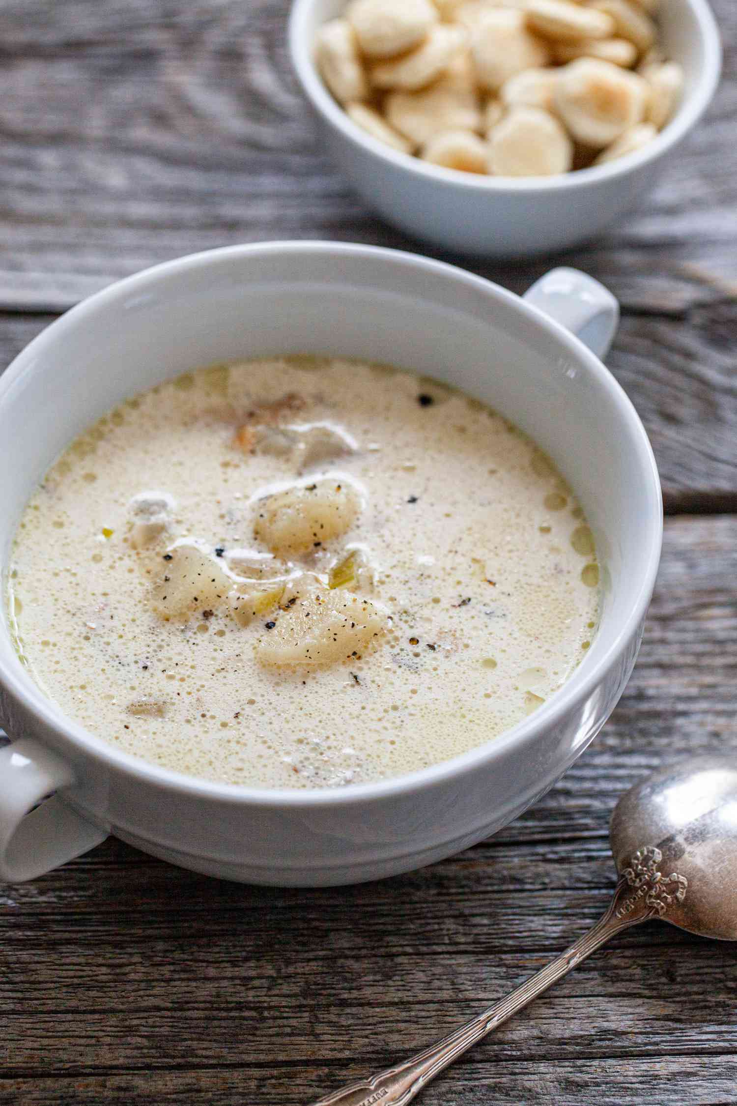 Bowl of Classic New England Chowder Next to a Small Bowl of Oyster Crackers and a Spoon