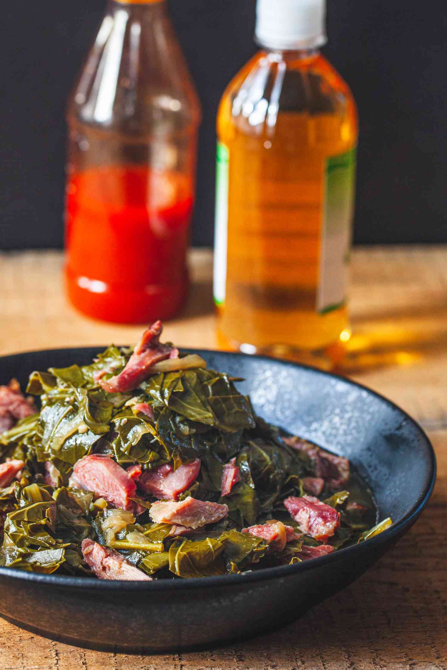 Side view of a bowl of southern collard greens served with condiments.