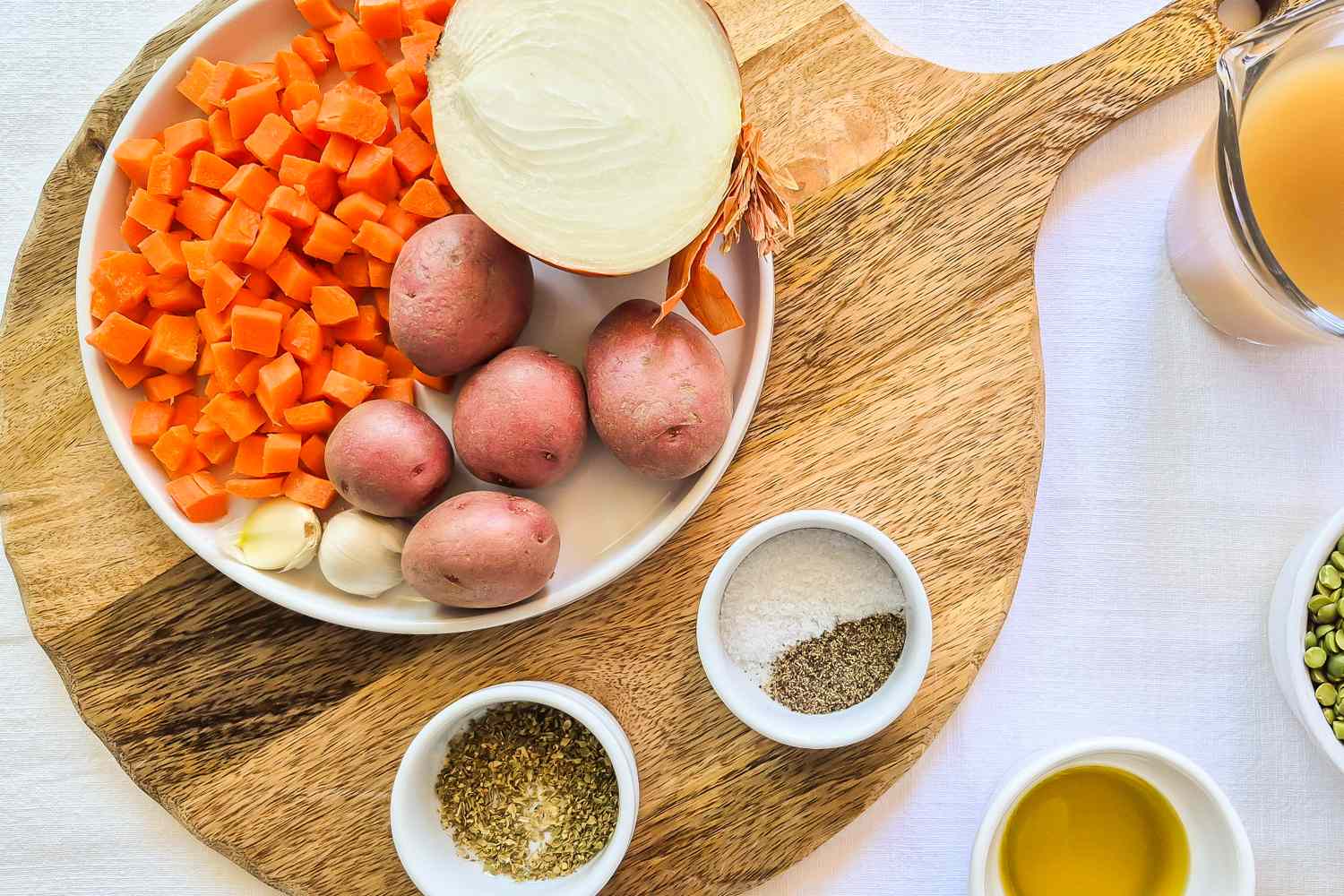 A set of ingredients including carrots potatoes an onion spices and broth prepared for soup on a wooden board