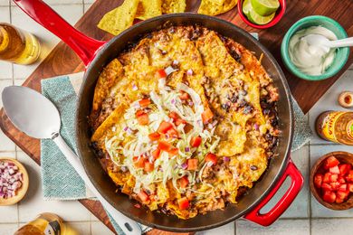 easy taco casserol in a pot at a table setting with bowls of toppings, chips on a platter, and a bottle of beer