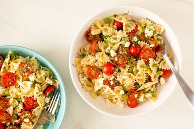 A serving of Greek pasta salad with cherry tomatoes and feta in a white bowl