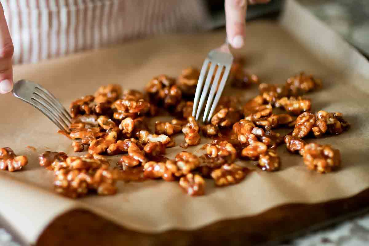 Two forks separating the walnuts on a piece of parchment paper