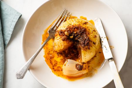 Whole cooked onion cut open served with sauce on a plate with a knife and fork