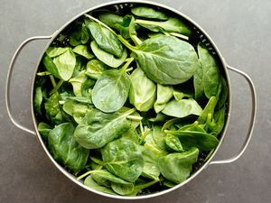 A colander filled with fresh spinach leaves