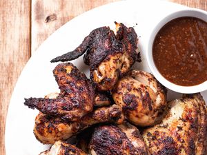 Overhead view of jerk chicken on a platter with dipping sauce.