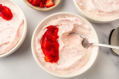 A bowl of strawberry mousse garnished with strawberry topping with additional bowls nearby