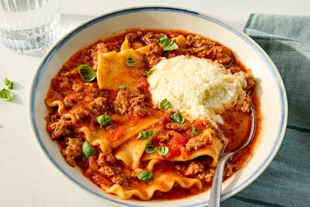 A bowl of lasagna soup topped with ricotta cheese and basil