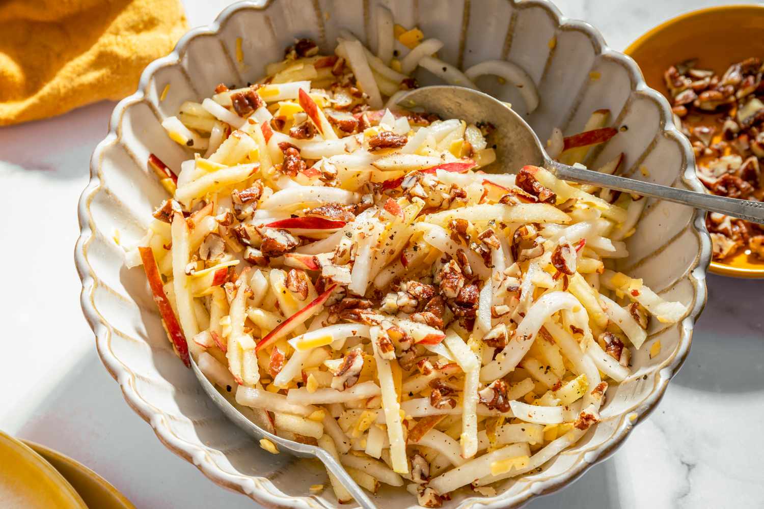 Kohlrabi and apple salad garnished with chopped nuts in a serving dish with a spoon