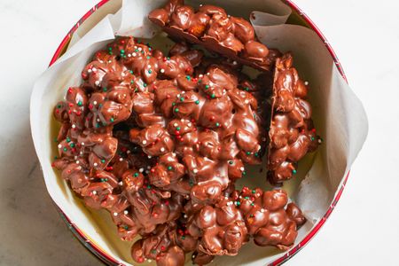 Chocolate candy clusters with nuts and sprinkles in a container lined with paper