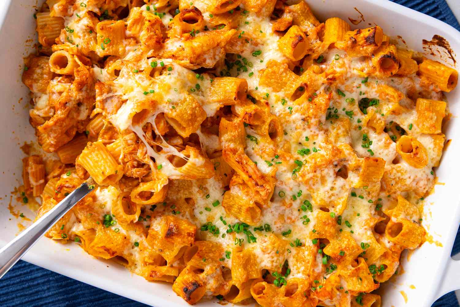 Baked pasta with chicken and cheese served in a white casserole dish topped with chopped chives