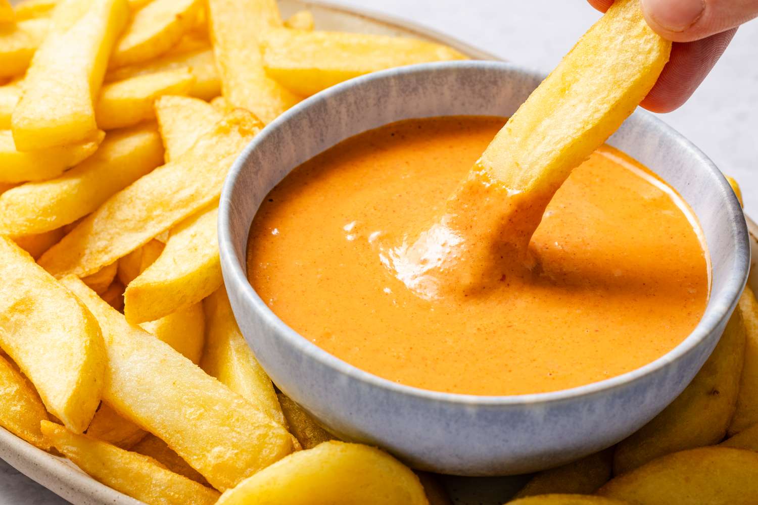 A bowl of sauce with French fries being dipped