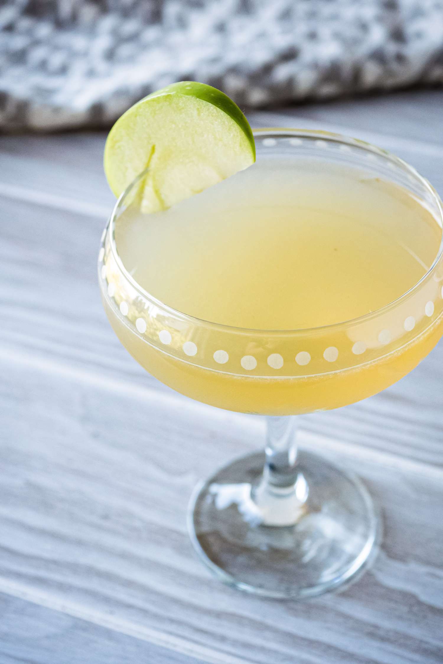 An easy appletini cocktail in a stemmed glass and garnished with a thin apple slice.